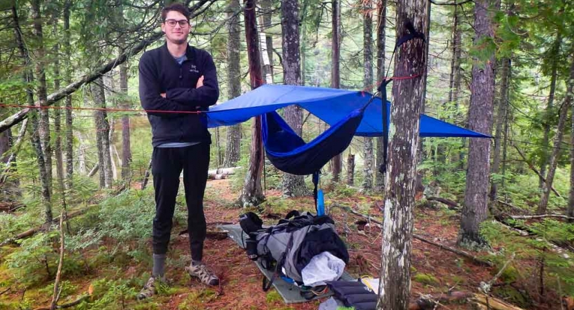 a person stands beside a shelter they made on an outward bound course in maine